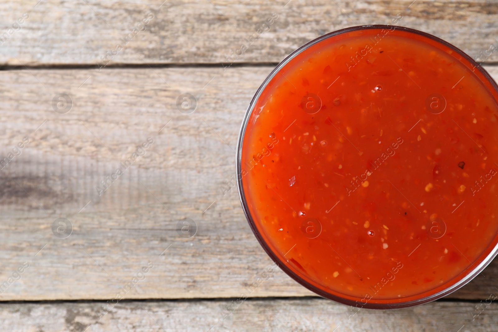 Photo of Spicy chili sauce in bowl on wooden table, top view. Space for text