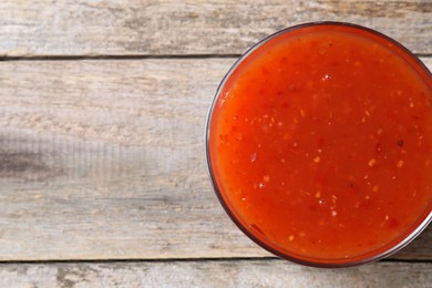 Photo of Spicy chili sauce in bowl on wooden table, top view. Space for text