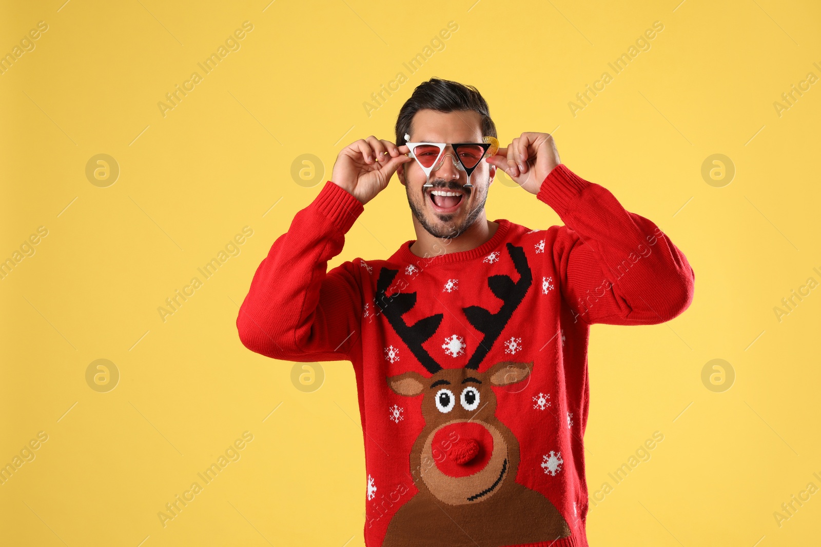 Photo of Happy man in Christmas sweater and party glasses on yellow background