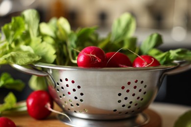 Metal colander with fresh radishes on table, closeup