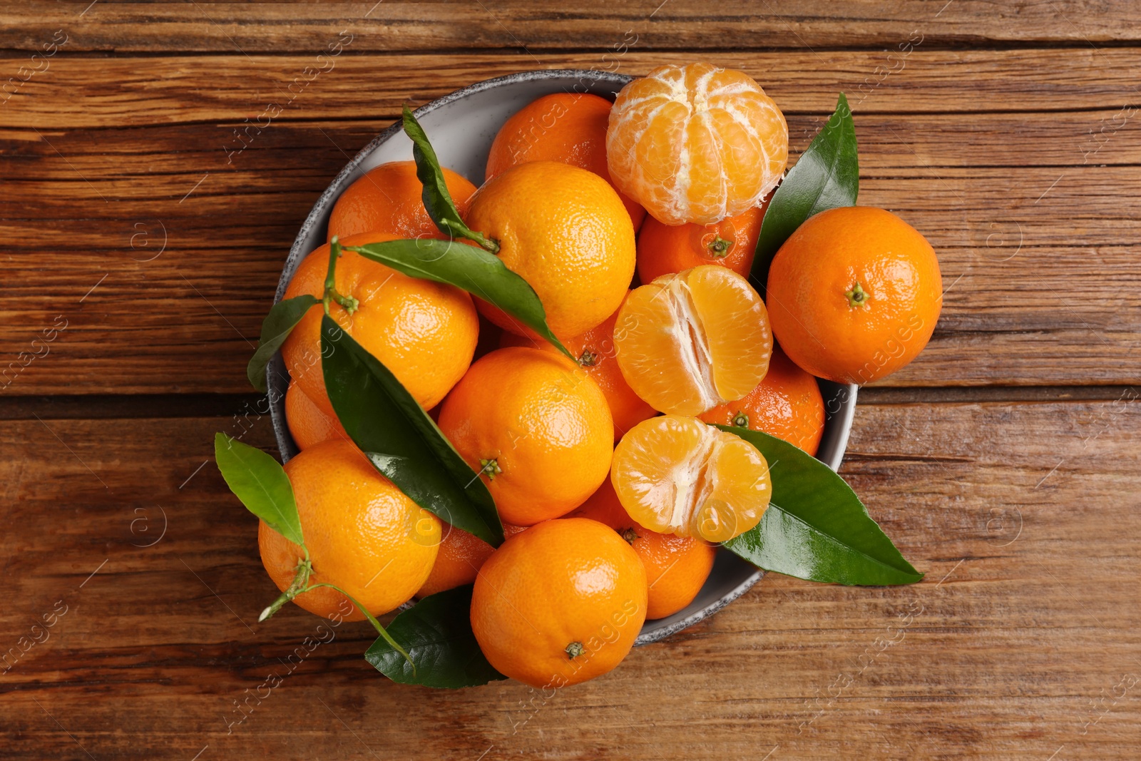 Photo of Fresh tangerines with green leaves in bowl on wooden table, top view
