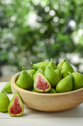 Cut and whole fresh green figs on white wooden table against blurred background, space for text