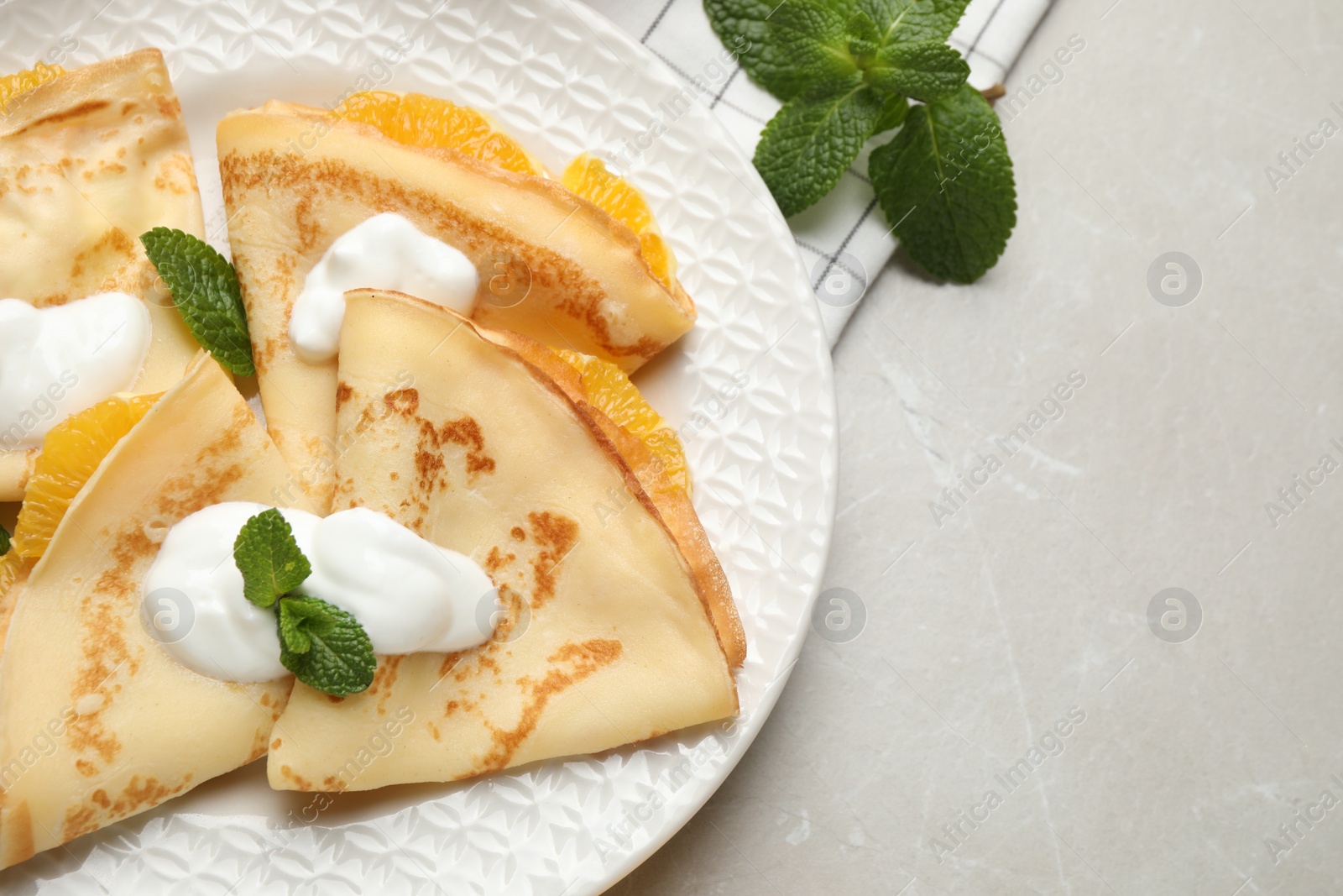 Photo of Delicious thin pancakes with oranges and cream on light table, flat lay