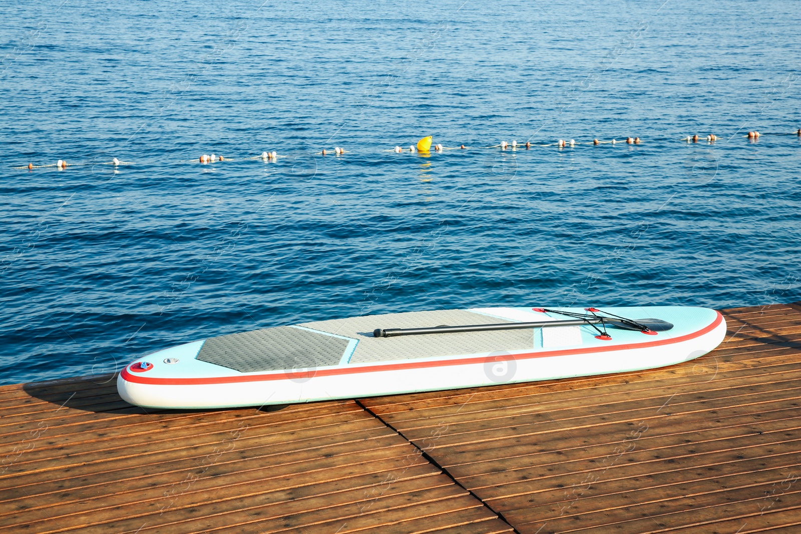 Photo of SUP board with paddle on wooden pier near sea