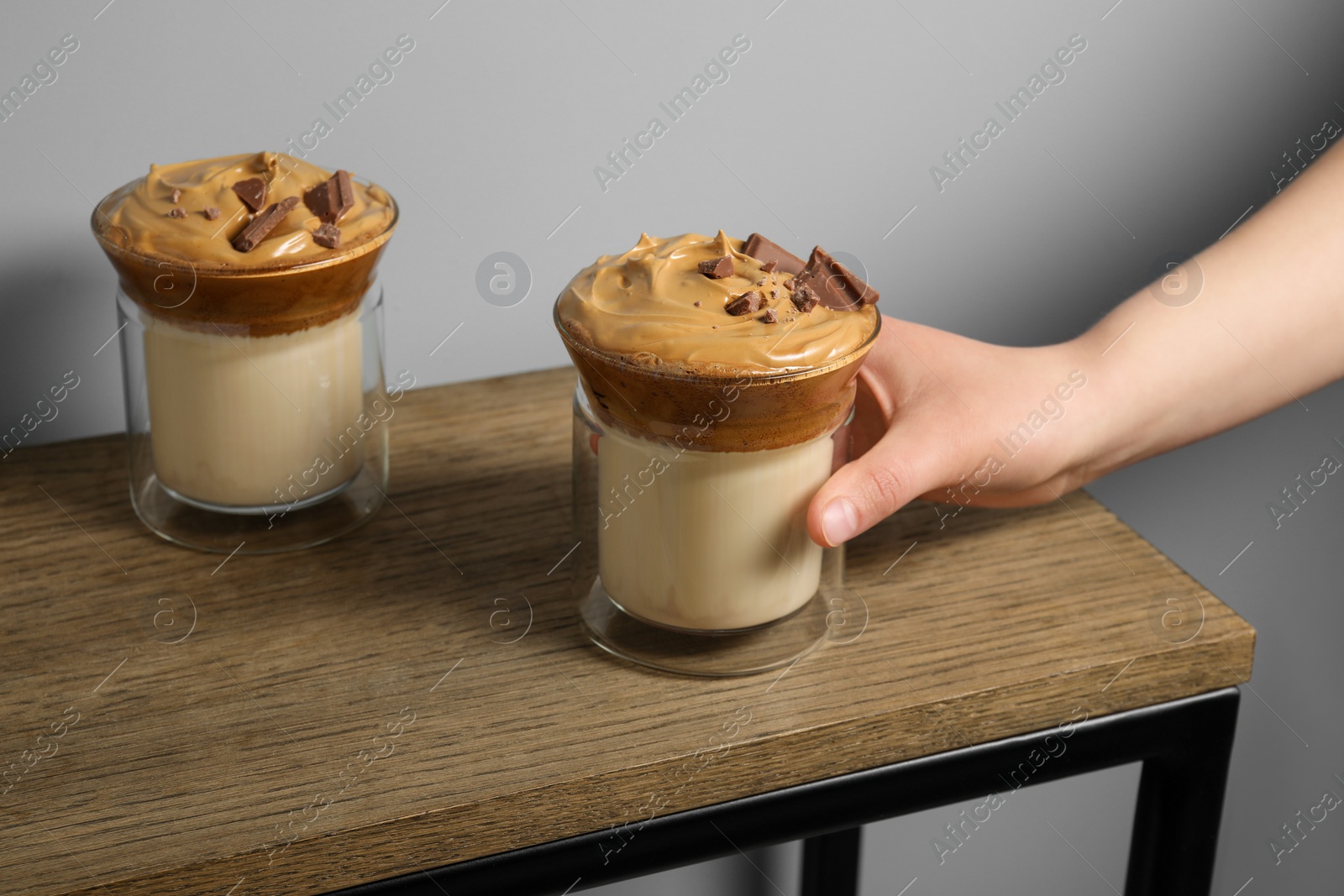 Photo of Woman taking glass of delicious dalgona coffee with chocolate from wooden table, closeup