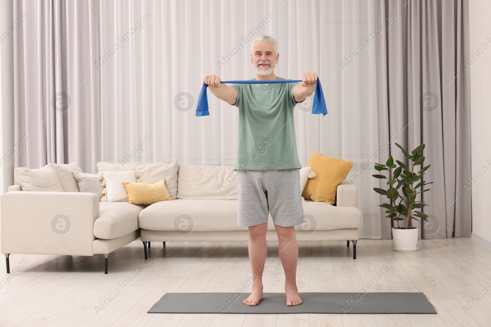 Photo of Senior man doing exercise with fitness elastic band on mat at home