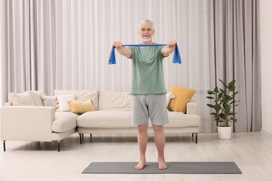 Photo of Senior man doing exercise with fitness elastic band on mat at home