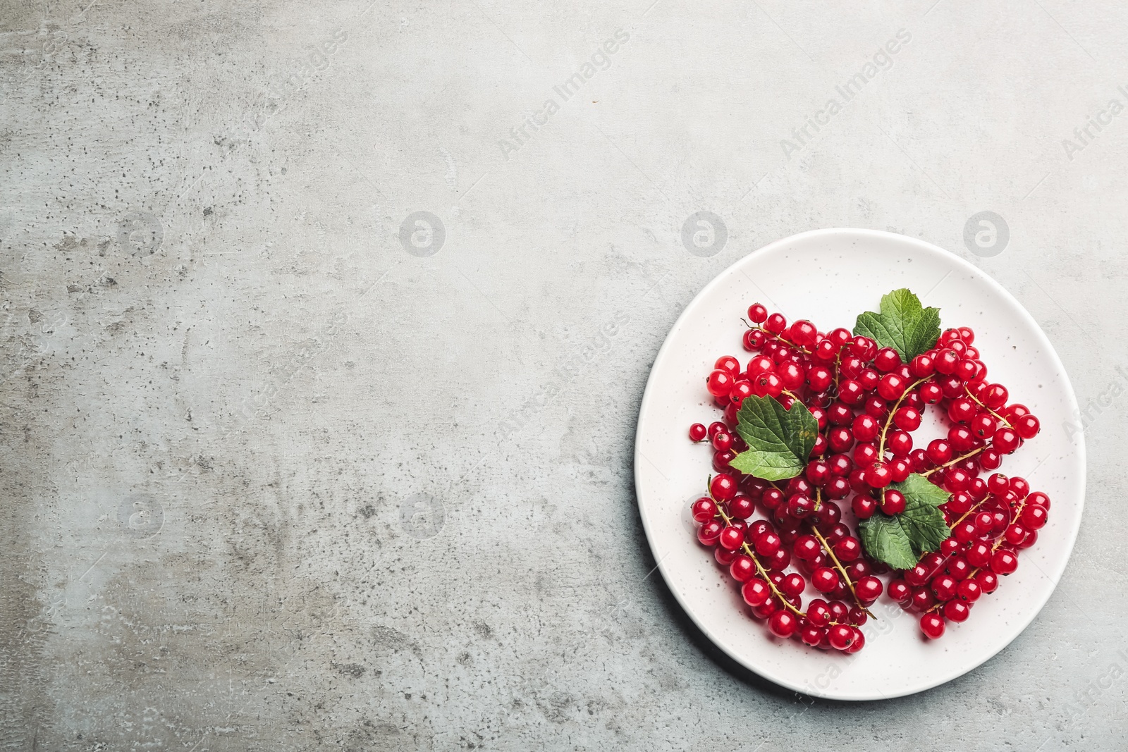 Photo of Delicious red currants and leaves on light grey table, top view. Space for text