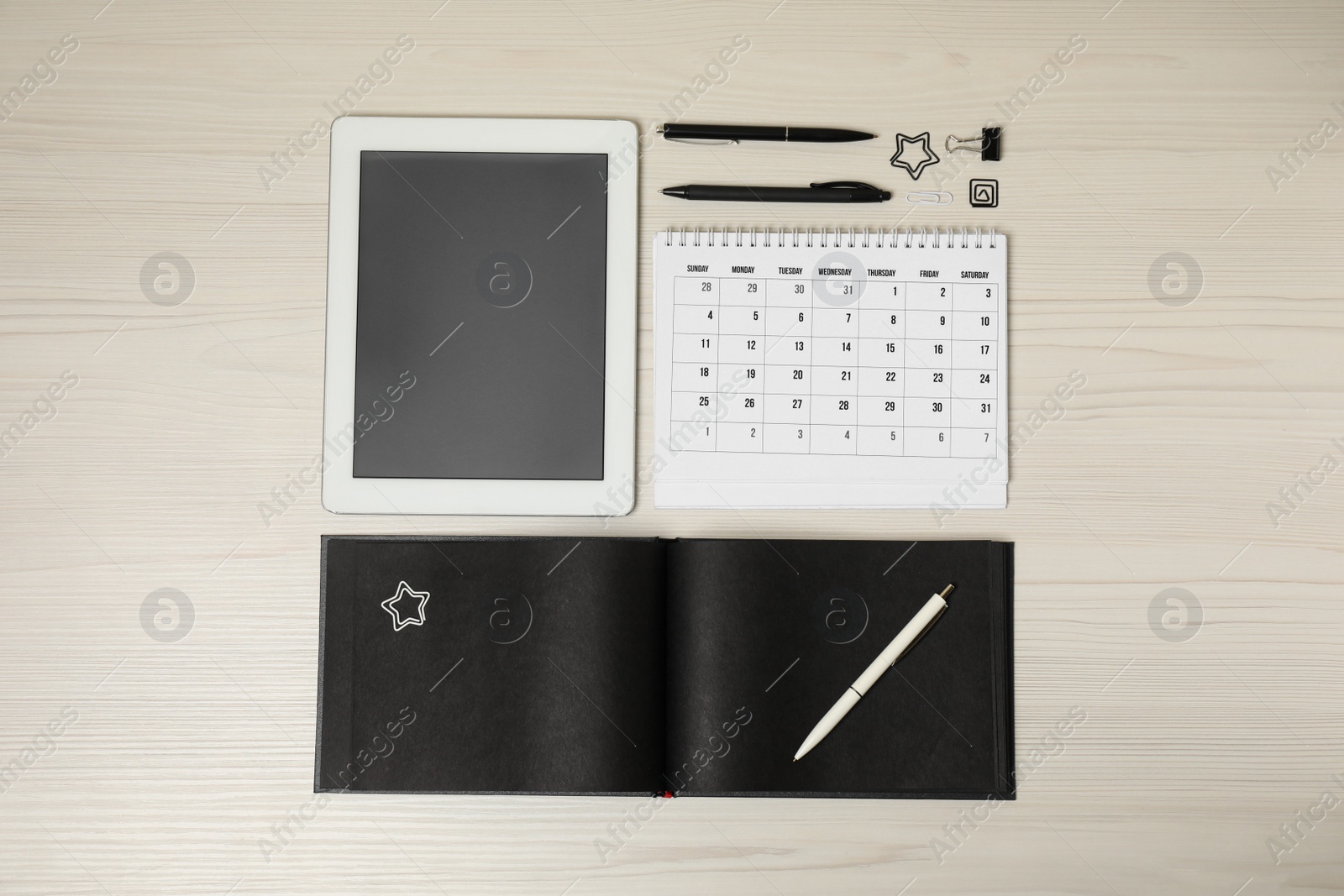 Photo of Calendar, notebook, tablet and stationery on wooden table, flat lay