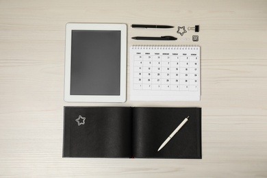 Calendar, notebook, tablet and stationery on wooden table, flat lay