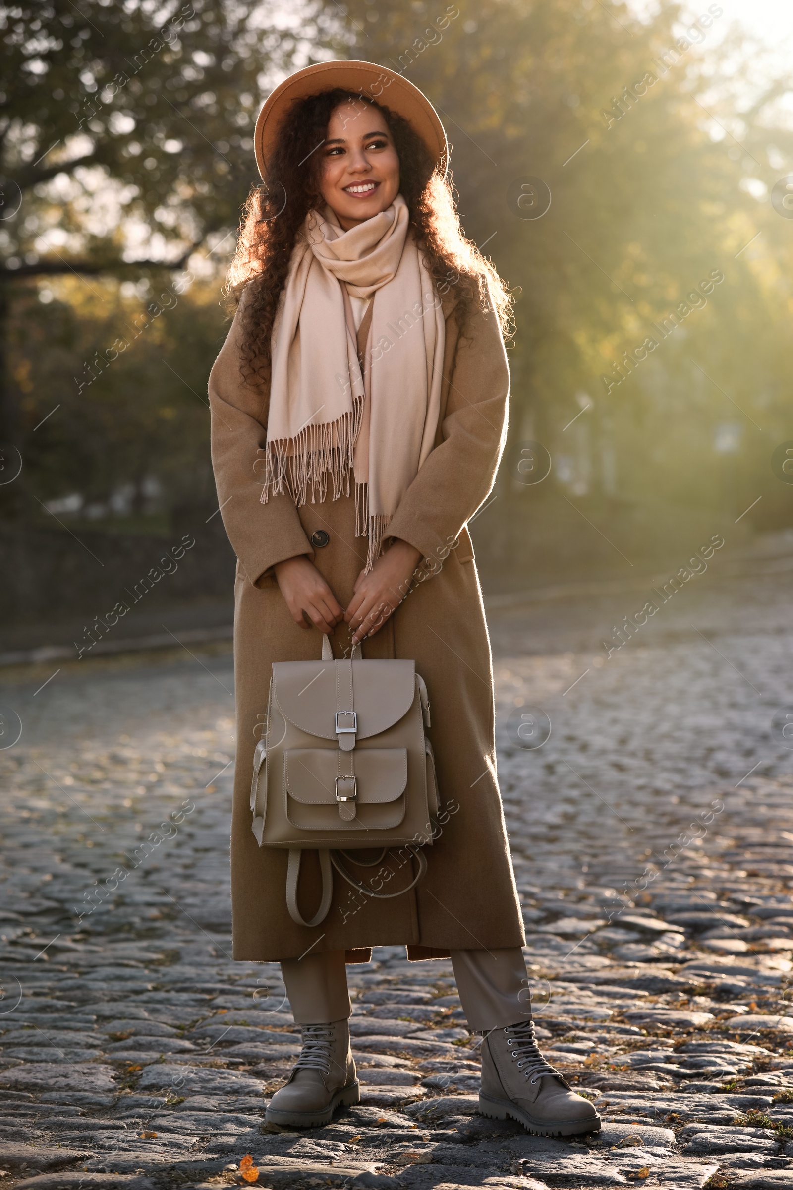 Photo of Full length portrait of beautiful African-American woman with stylish beige backpack on city street