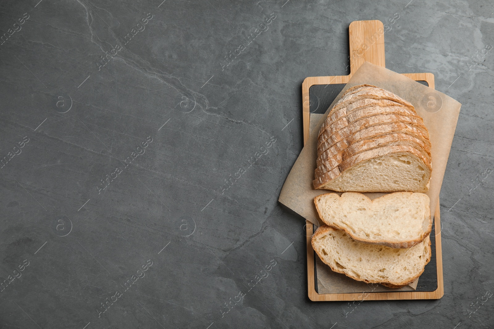 Photo of Board with cut bread on grey table, top view. Space for text