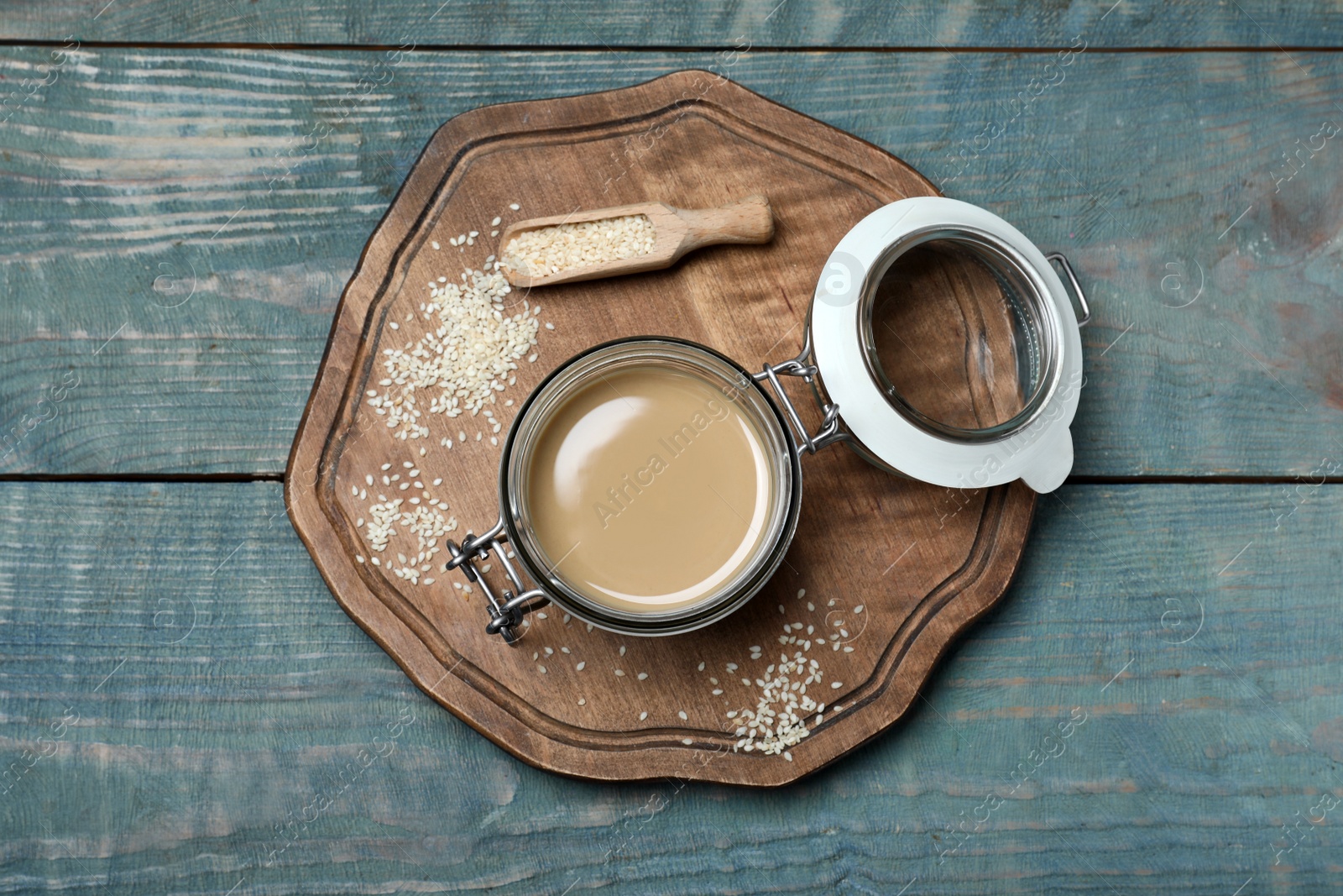 Photo of Jar of tasty sesame paste and seeds on light blue wooden table, top view