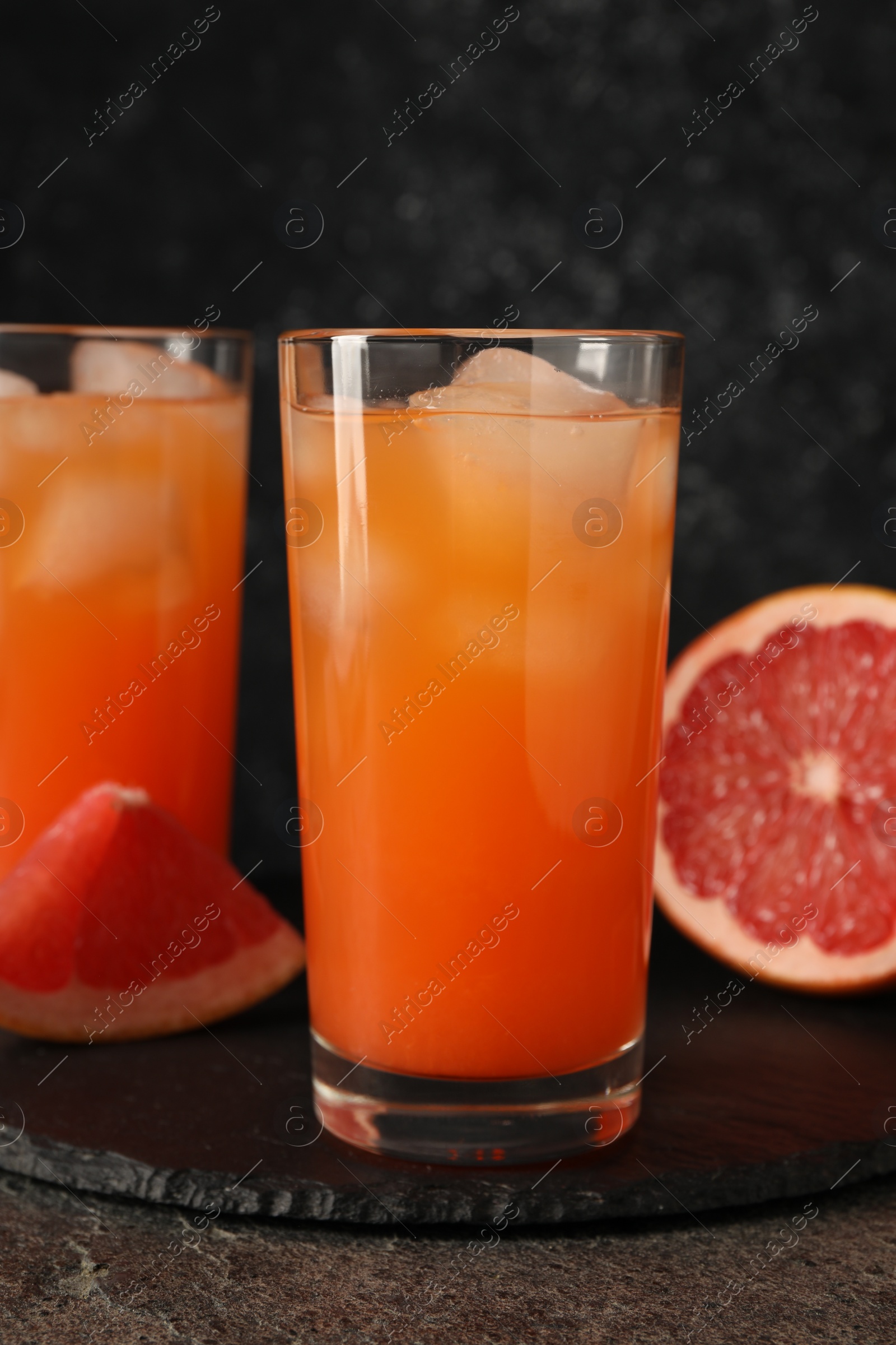 Photo of Tasty grapefruit drink with ice in glasses and fresh fruits on dark textured table