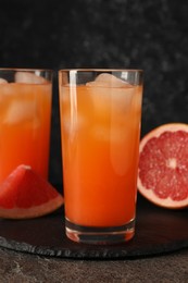 Photo of Tasty grapefruit drink with ice in glasses and fresh fruits on dark textured table