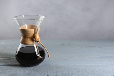 Photo of Glass chemex coffeemaker with drip coffee on grey wooden table. Space for text