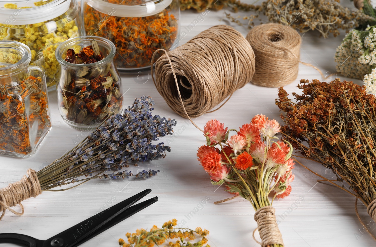 Photo of Different medicinal herbs, scissors and spools on white wooden table