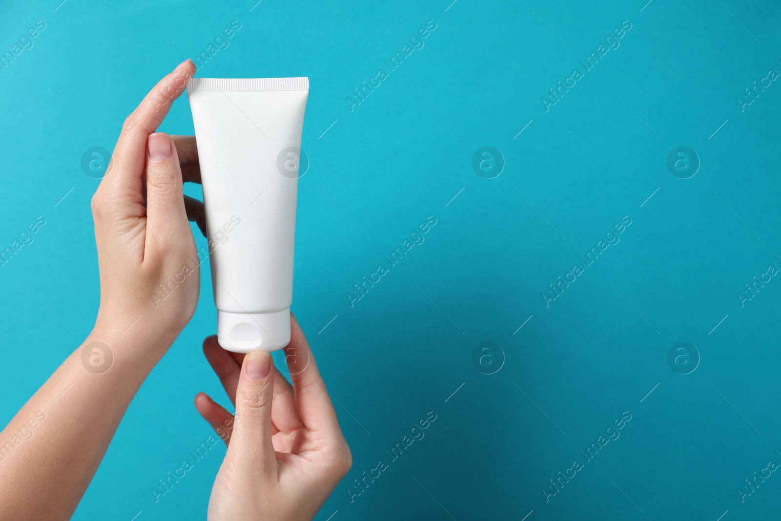 Photo of Woman with tube of hand cream on light blue background, closeup. Space for text