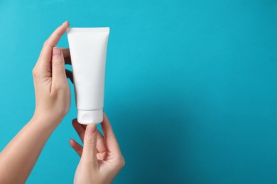 Woman with tube of hand cream on light blue background, closeup. Space for text