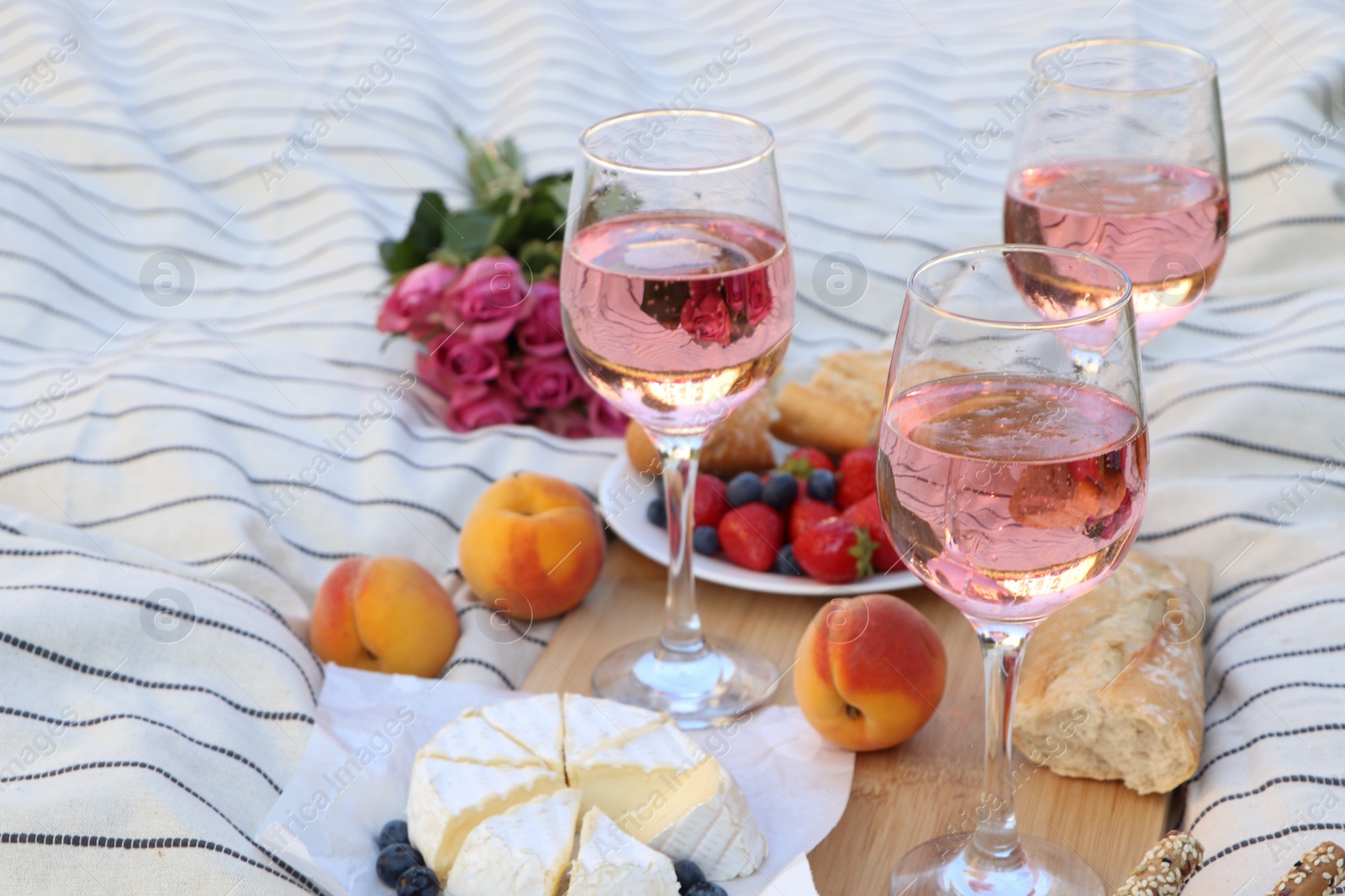 Photo of Glasses of delicious rose wine, flowers and food on white picnic blanket