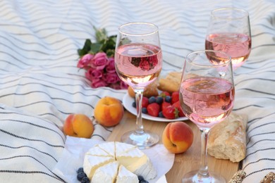 Glasses of delicious rose wine, flowers and food on white picnic blanket