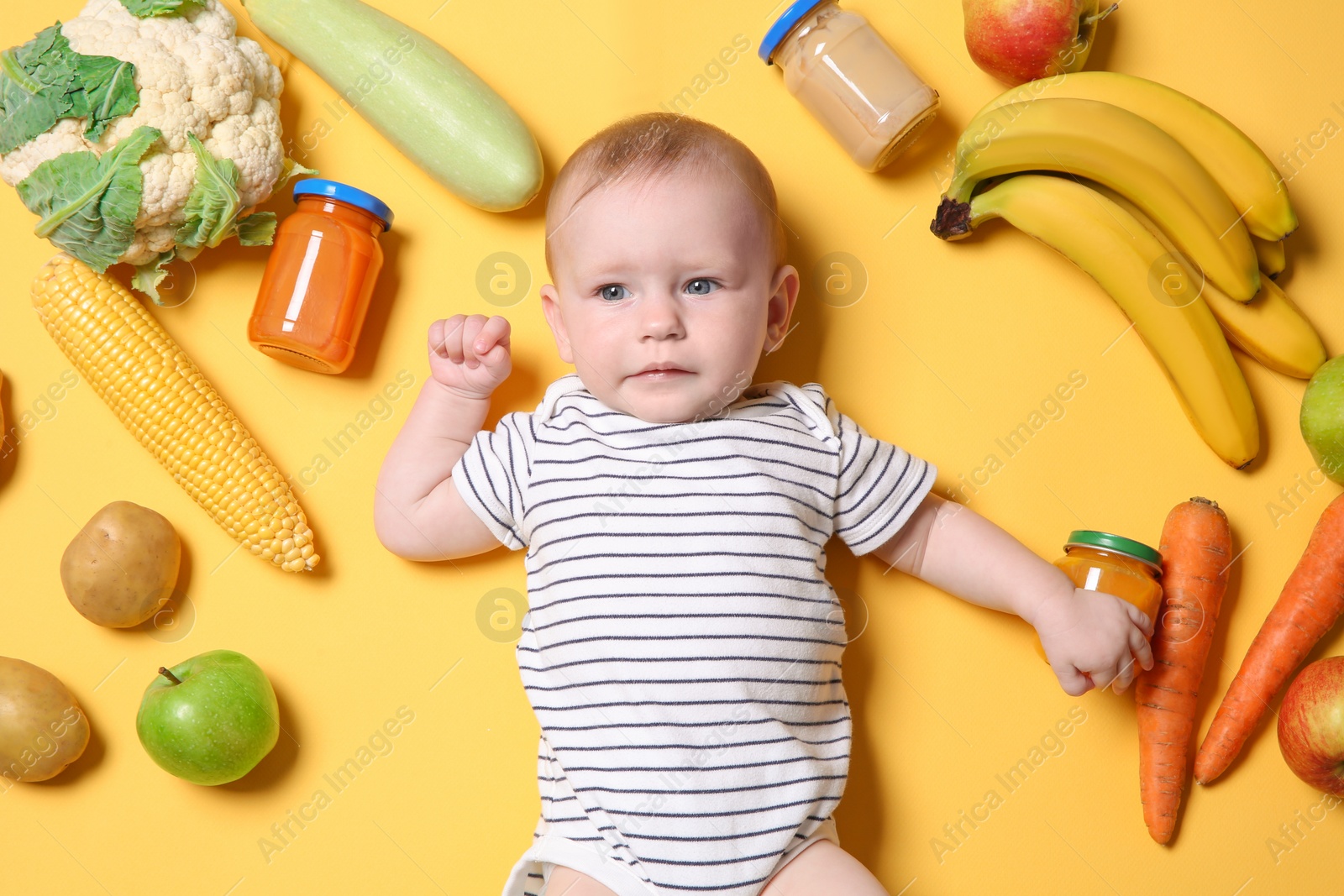 Photo of Cute little child with ingredients and purees in jars on color background, top view. Baby food