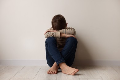 Child abuse. Upset boy sitting on floor near beige wall indoors