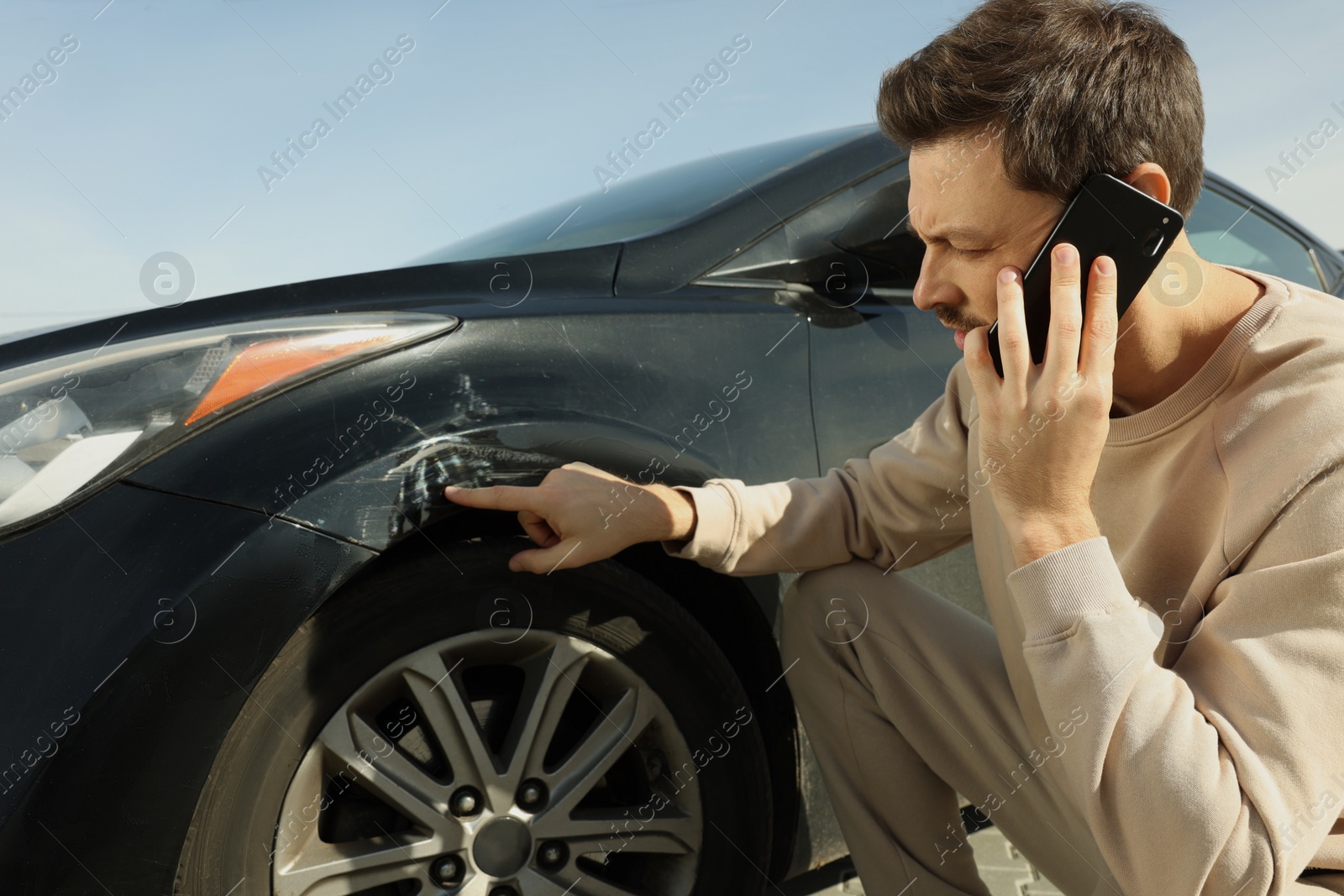 Photo of Man talking on phone near car with scratch outdoors