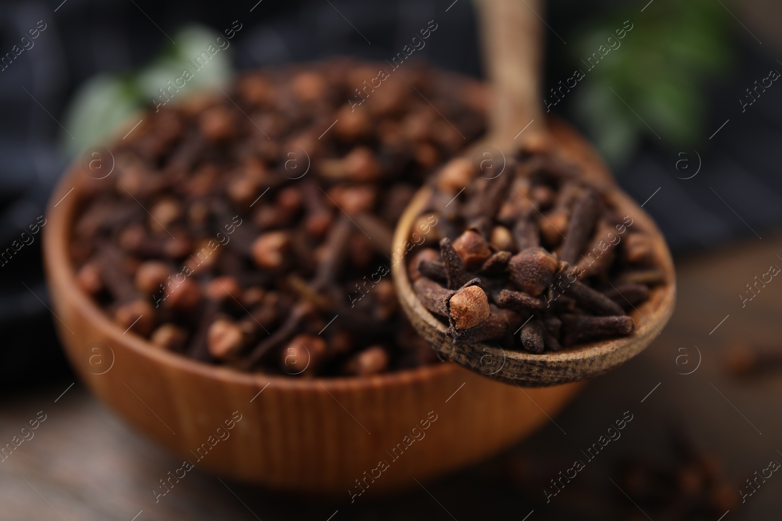 Photo of Bowl and spoon with aromatic cloves on wooden table, closeup