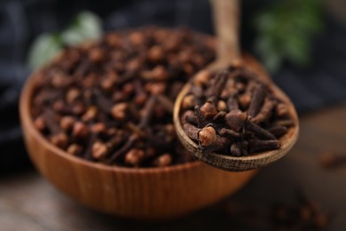 Bowl and spoon with aromatic cloves on wooden table, closeup