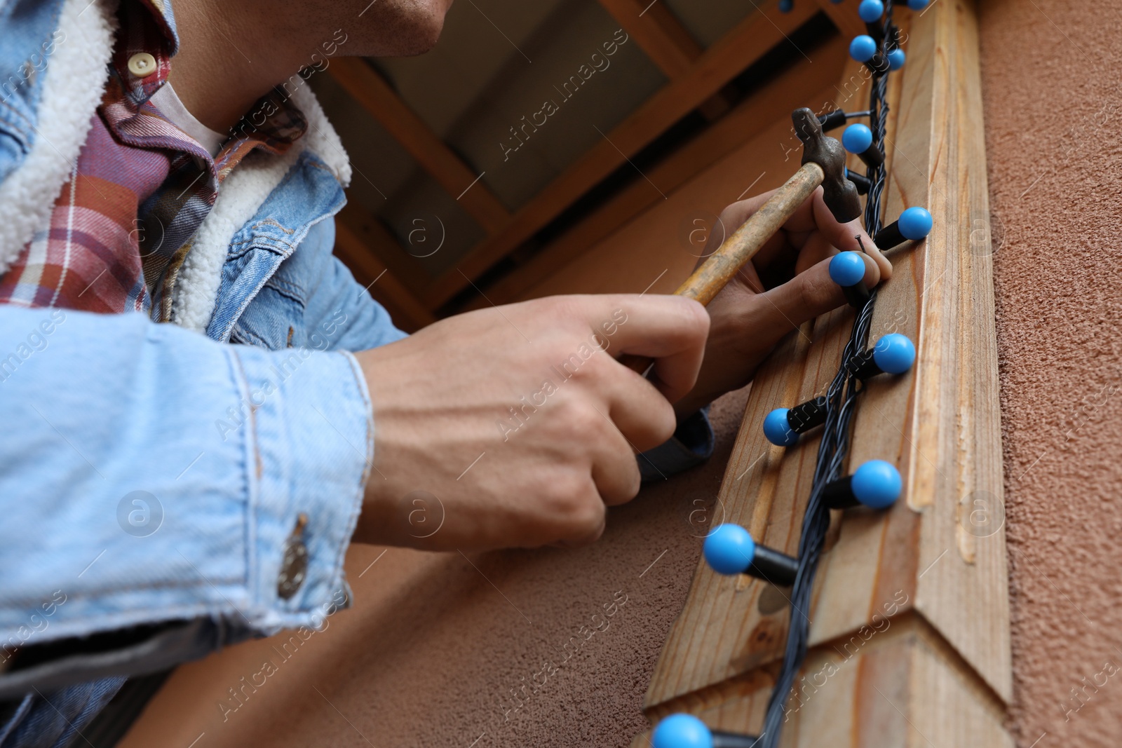 Photo of Man decorating house with Christmas lights outdoors, closeup