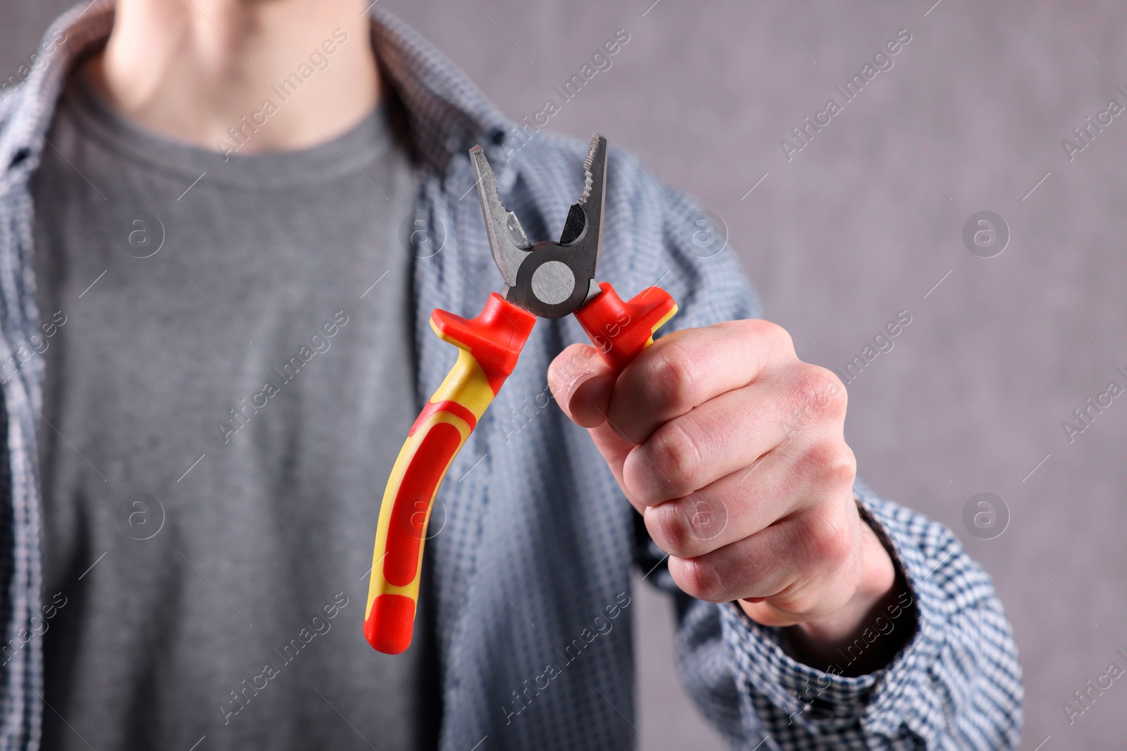 Photo of Young man holding pliers on grey background, closeup