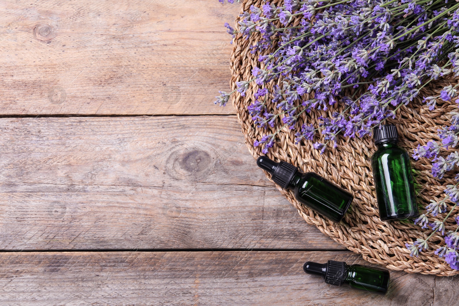 Photo of Bottles of essential oil and lavender flowers on wooden background, flat lay. Space for text