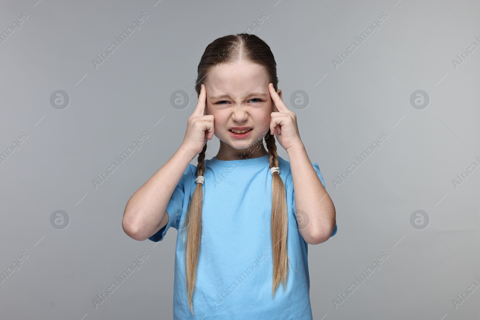 Photo of Little girl suffering from headache on grey background