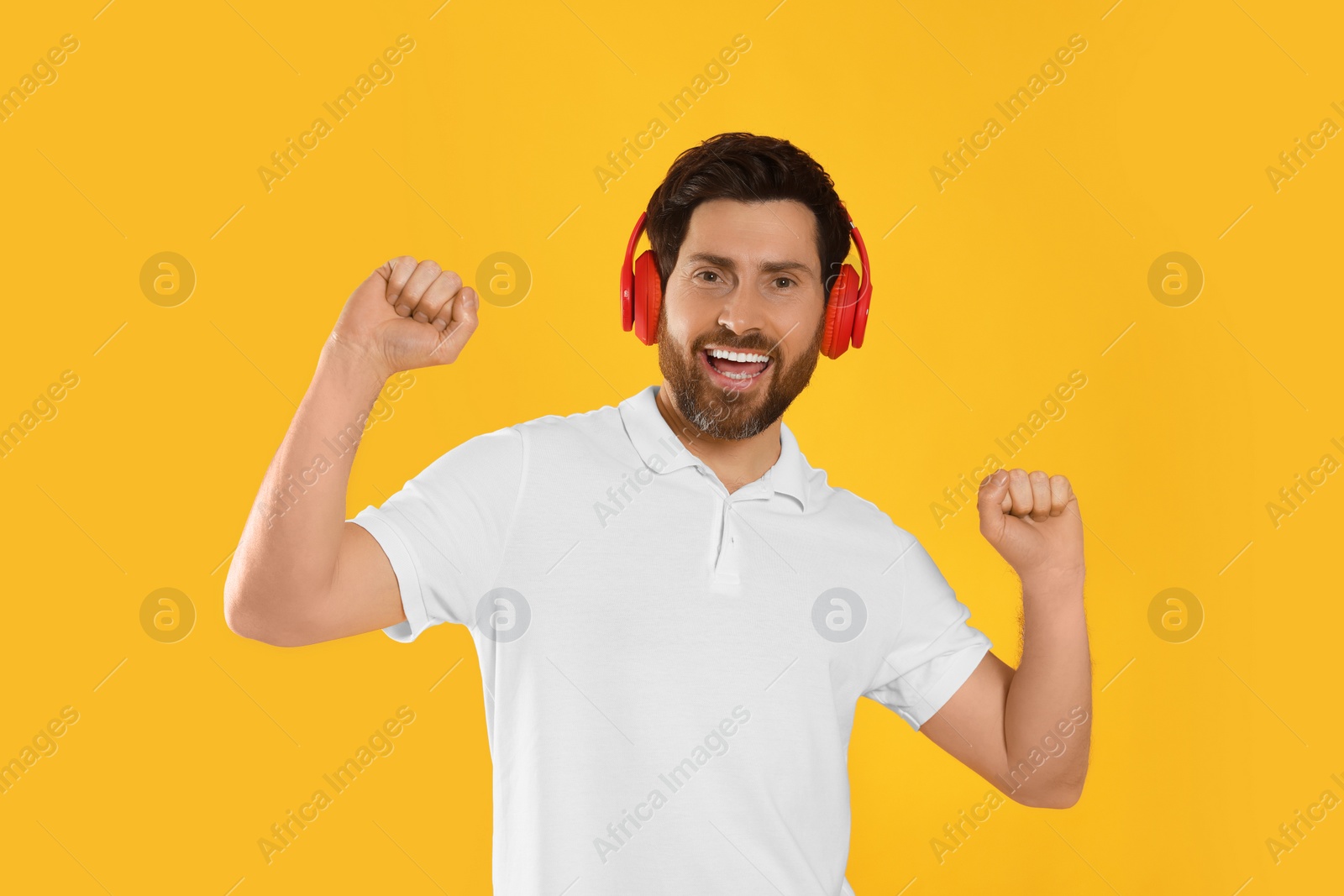 Photo of Happy man listening music with headphones on yellow background