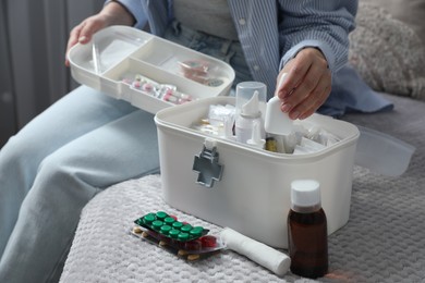 Photo of Woman putting medicament into first aid kit indoors, closeup