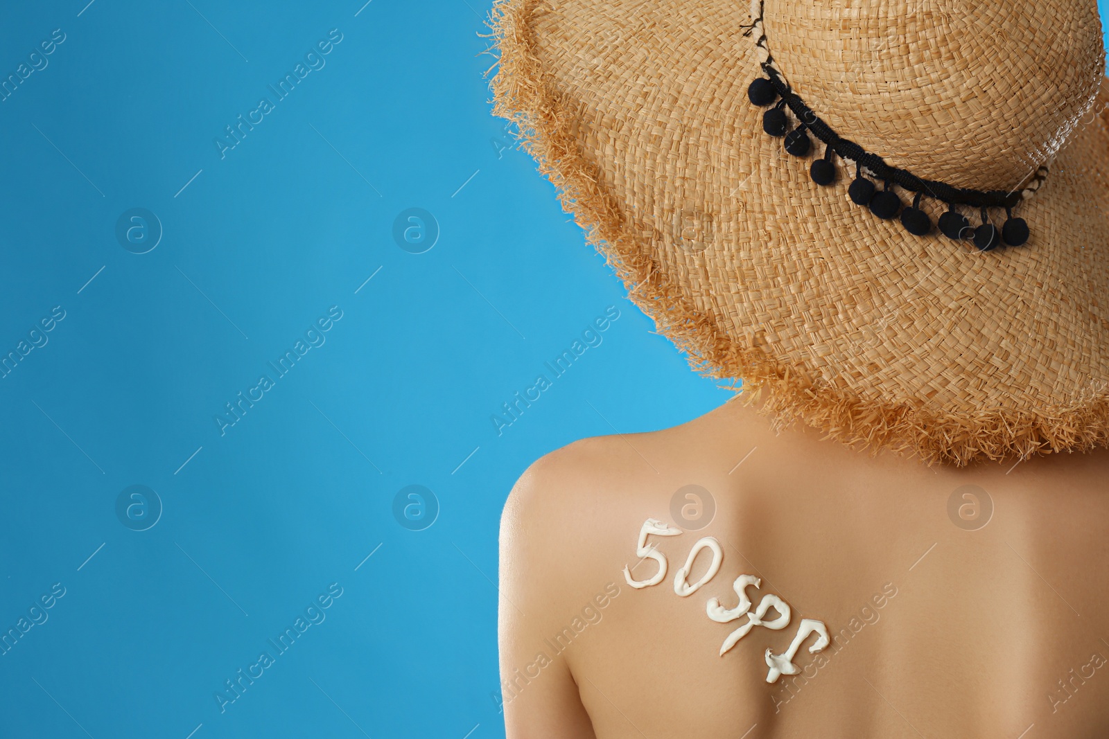Photo of 50 SPF written with sun protection cream on woman's back against light blue background. Space for text