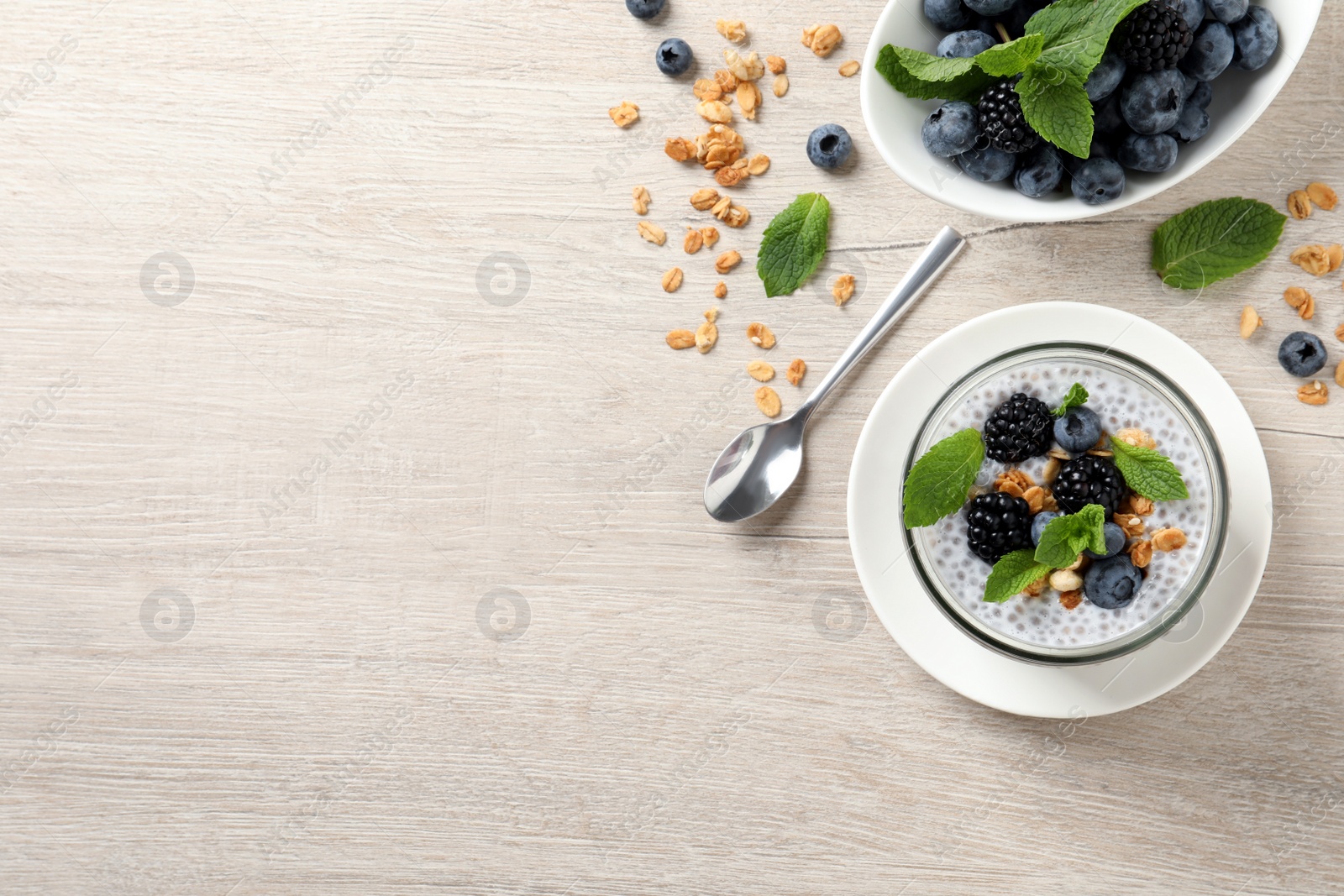 Photo of Delicious chia pudding with berries and granola on wooden table, flat lay. Space for text