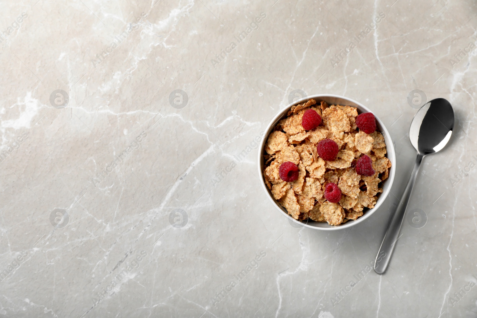 Photo of Bowl of cornflakes with raspberries on light table, top view with space for text