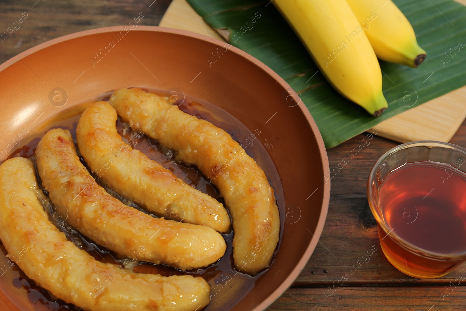 Photo of Delicious fresh and fried bananas with rum on wooden table, closeup
