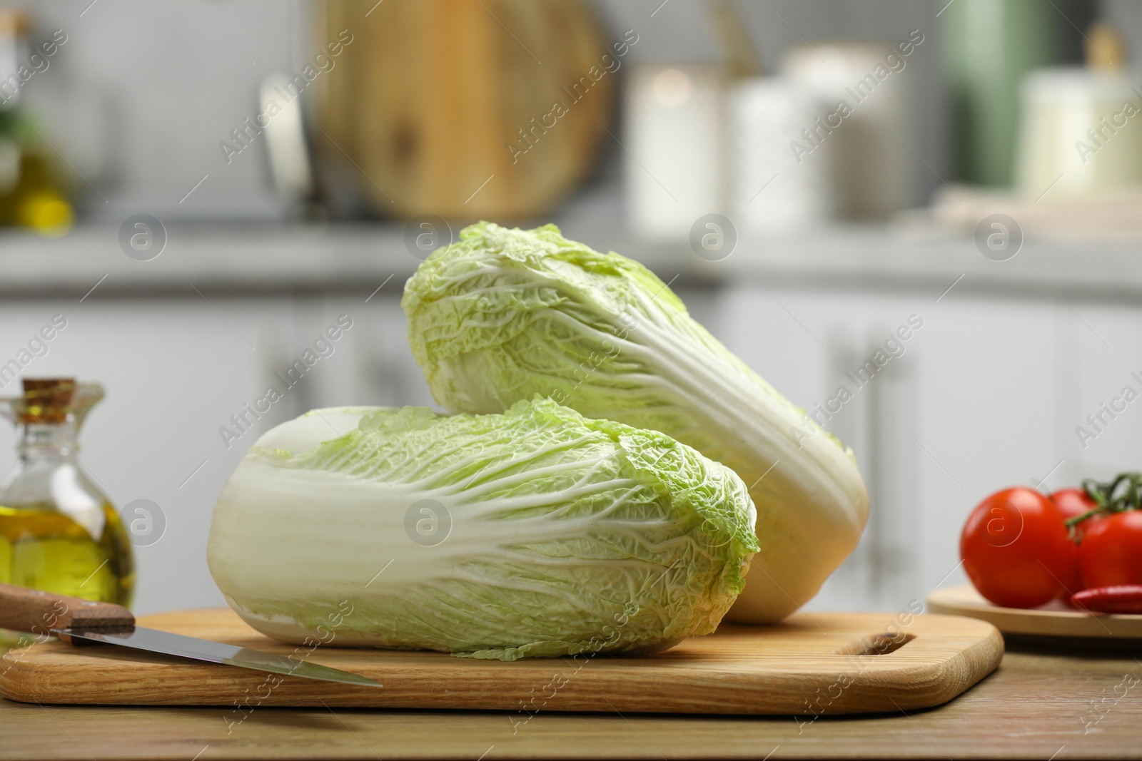 Photo of Fresh Chinese cabbages, knife, tomatoes and oil on wooden table in kitchen