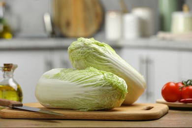 Photo of Fresh Chinese cabbages, knife, tomatoes and oil on wooden table in kitchen