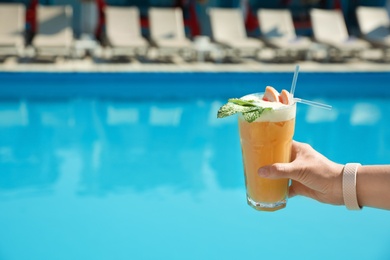 Woman with refreshing cocktail near swimming pool outdoors, closeup. Space for text