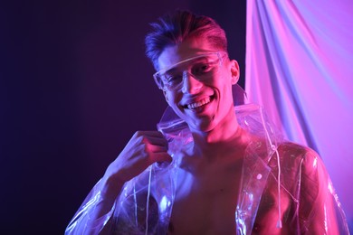 Photo of Stylish young man wearing clear coat and glasses in neon lights