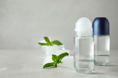 Photo of Roll-on deodorants and ice cubes with mint on light grey table, space for text