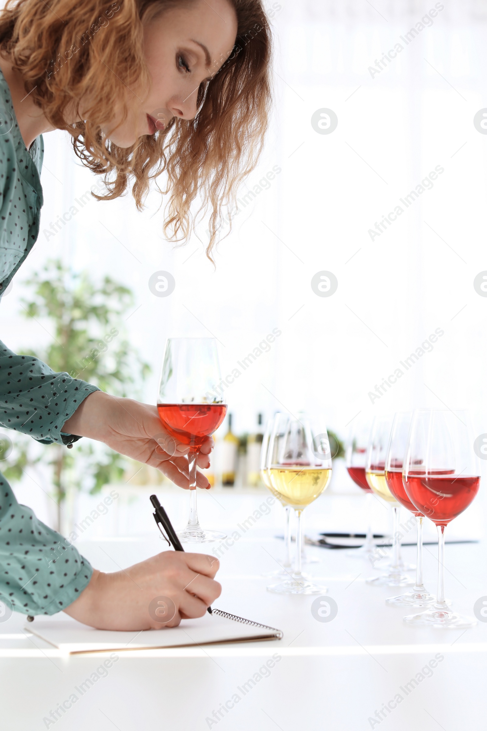 Photo of Woman with notebook tasting delicious wine at table indoors