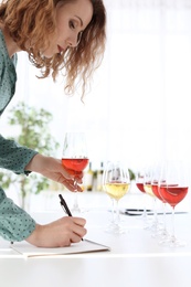 Woman with notebook tasting delicious wine at table indoors