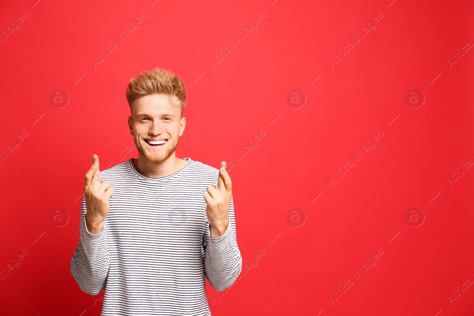 Photo of Portrait of hopeful man with crossed fingers on red background, space for text