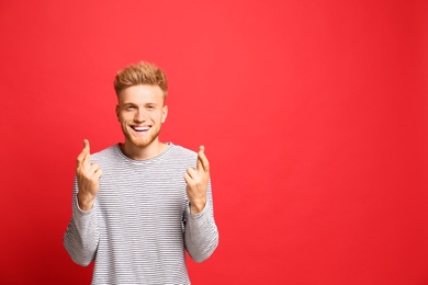 Portrait of hopeful man with crossed fingers on red background, space for text