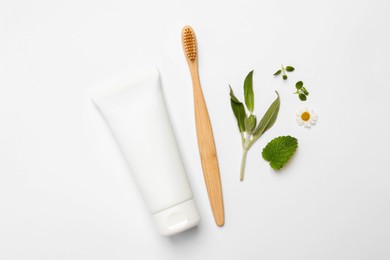 Bamboo toothbrush, tube of cream and herbs on white background, flat lay